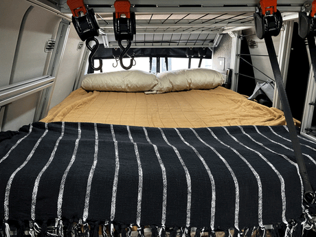 Inside an RV rental: A tidy bed with pillows and a striped blanket, plus handy overhead storage.