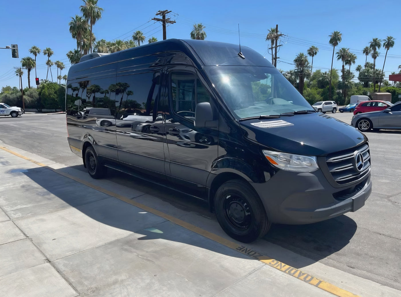 A sleek black Mercedes-Benz Sprinter van, perfect for an RV rental, parked in a sunny loading zone under palm trees. — photo 2
