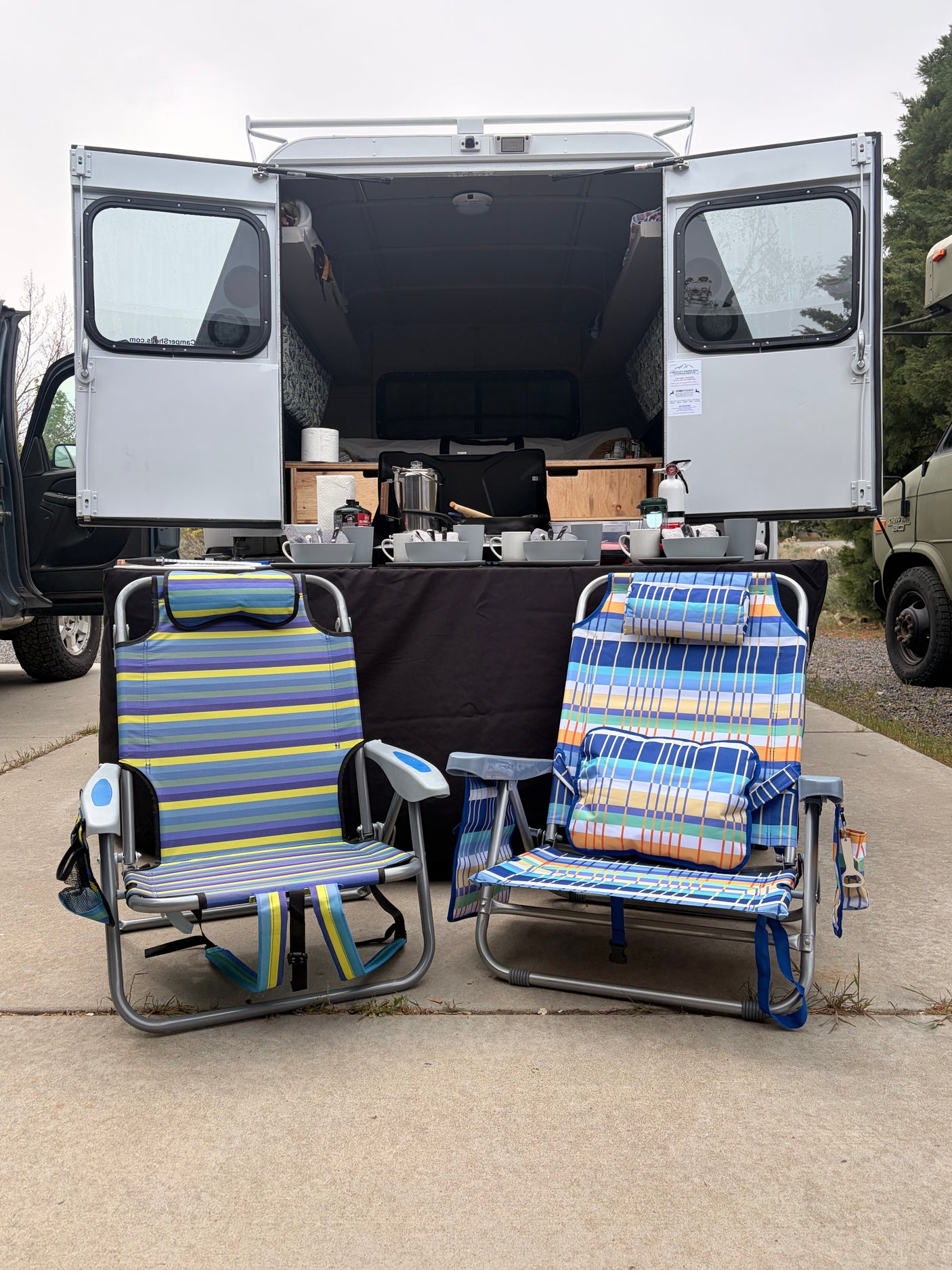 RV rental: Camper van with rear doors open, revealing a cozy interior & outdoor kitchen setup with chairs.