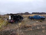 Off-road adventure in the desert: blue truck & rugged RV rental trailer setup with awning for comfortable camping.