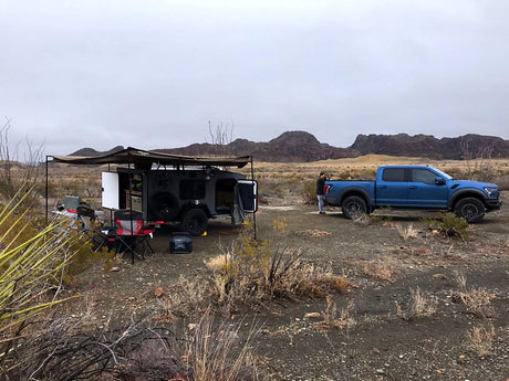 Off-road adventure in the desert: blue truck & rugged RV rental trailer setup with awning for comfortable camping.