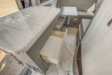 Modern RV rental interior: A light-toned kitchen counter, open drawer, and compact dining area. Functional and ready for travel.