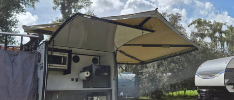 RV rental outdoor kitchen with extended awning, microwave, fridge, and paper towel dispenser, perfect for camping.