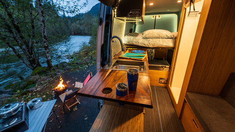 This cozy rv rental camper van kitchen and bedroom open to a riverside campfire. Perfect for outdoor adventure and van life!