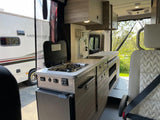 Explore mobile living! This rv rental interior boasts a compact kitchen with a stove, sink, and fridge, plus a passenger seat.