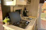 RV rental kitchen: stovetop, sink, and plant, with a desert landscape visible outside. Ready for adventure!
