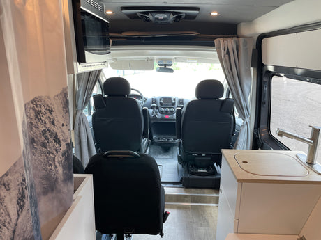 RV rental interior view from rear: cockpit with seats & dashboard, kitchenette, & microwave. Ready for road trips.
