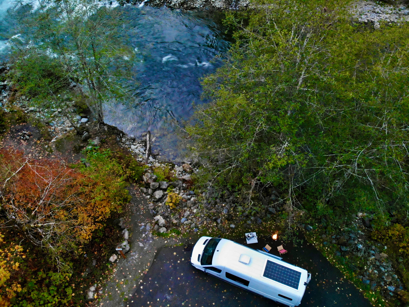 RV rental campervan with solar panel parked riverside, enjoying a campfire and chairs. Perfect for outdoor adventure!