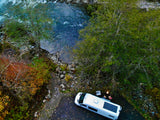RV rental campervan with solar panel parked riverside, enjoying a campfire and chairs. Perfect for outdoor adventure!