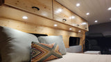 Inside a bright RV rental: wooden walls, overhead cabinets, a cozy bed, and a compact sink. Ideal mobile living.