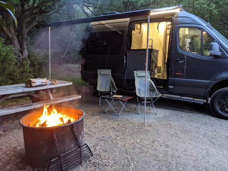Evening relaxation at an rv rental campsite with a warm campfire, open van, and inviting outdoor seating.