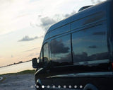 Scenic RV rental: Dark van by serene water at sunset, clouds reflecting in windows.
