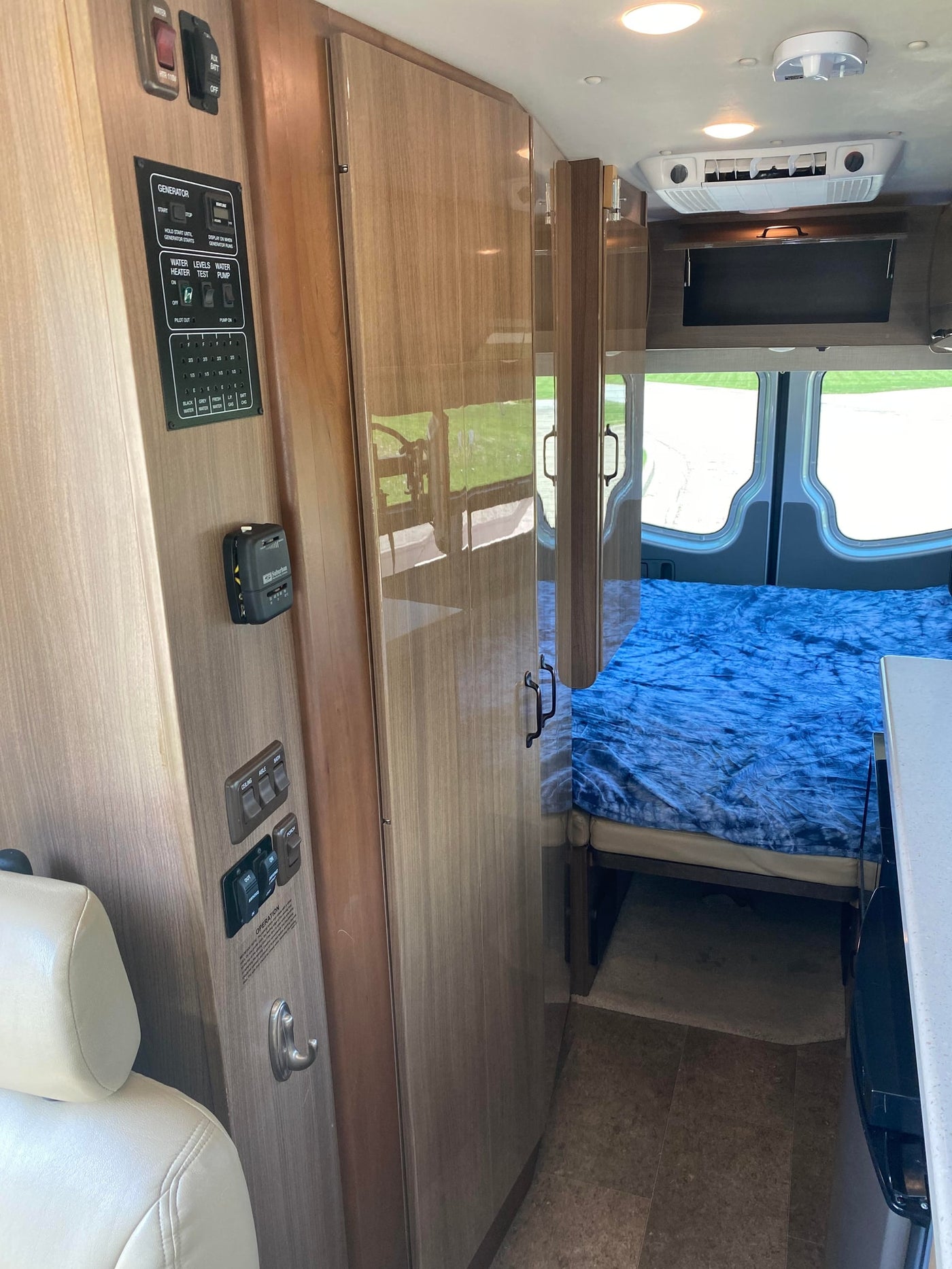 RV rental interior: control panel for generator, water, and lights, with a bed, wood cabinetry, and ceiling-mounted AC. — photo 9