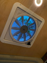 RV rental essential: A ceiling fan with integrated light and clear controls. Blue sky and green trees are visible through the fan's mesh.
