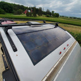 Top of an RV rental with roof-mounted solar panels and racks, parked in a rural setting.