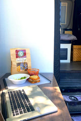 RV rental mobile office setup: A laptop next to a sandwich, tortilla chips, salsa, and broccoli.
