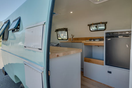 RV rental interior: light blue camper with bright kitchen, wood counters, stove, sink, & fridge. Ready for adventures!