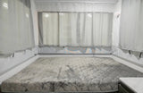 Cozy RV rental pop-up camper bed with a quilted mattress & sheer curtains, an exit sign visible on the right.