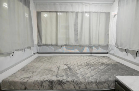 Cozy RV rental pop-up camper bed with a quilted mattress & sheer curtains, an exit sign visible on the right.