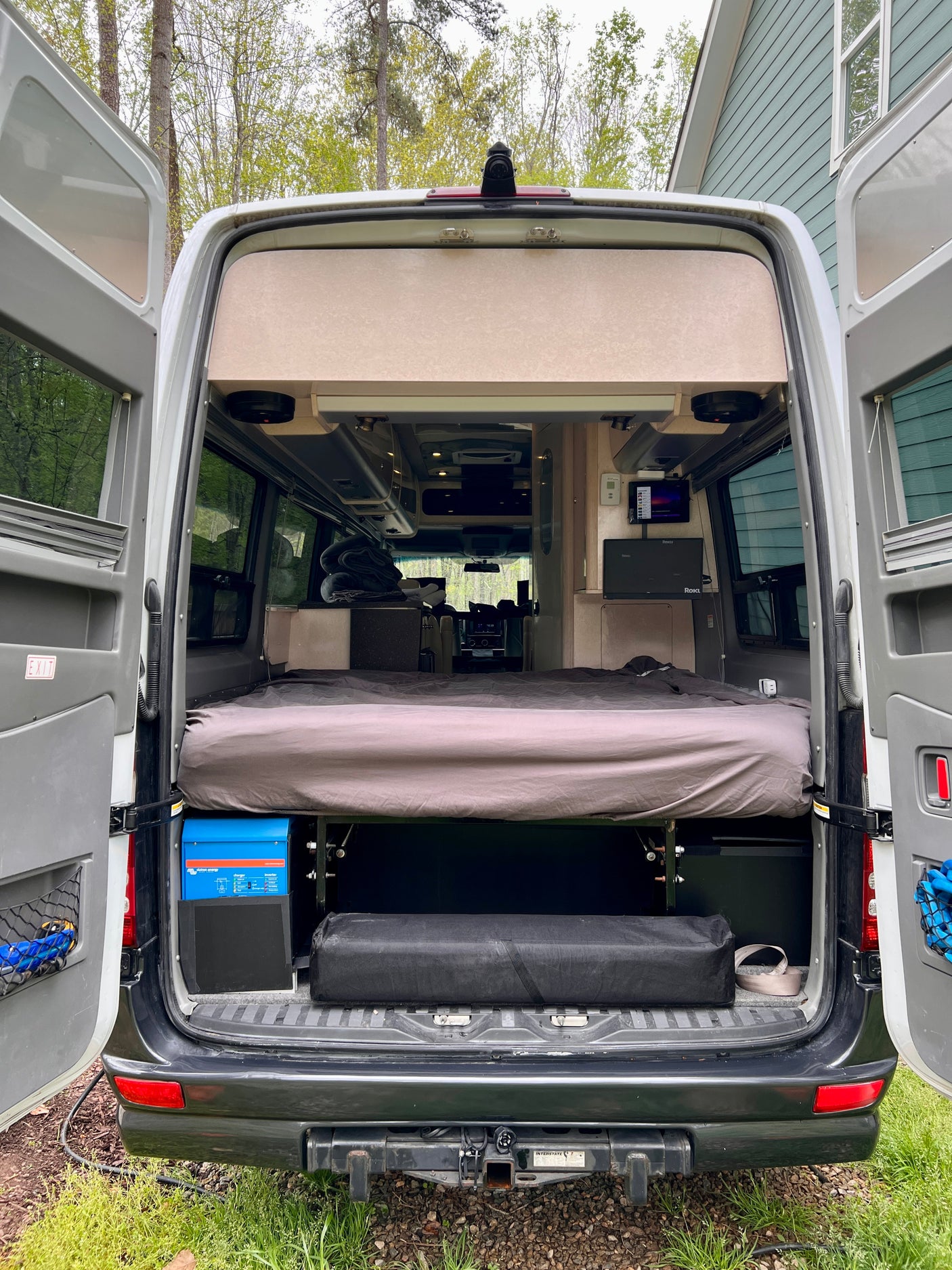 Spacious RV rental interior from the rear: bed, power system, and storage with open back doors.