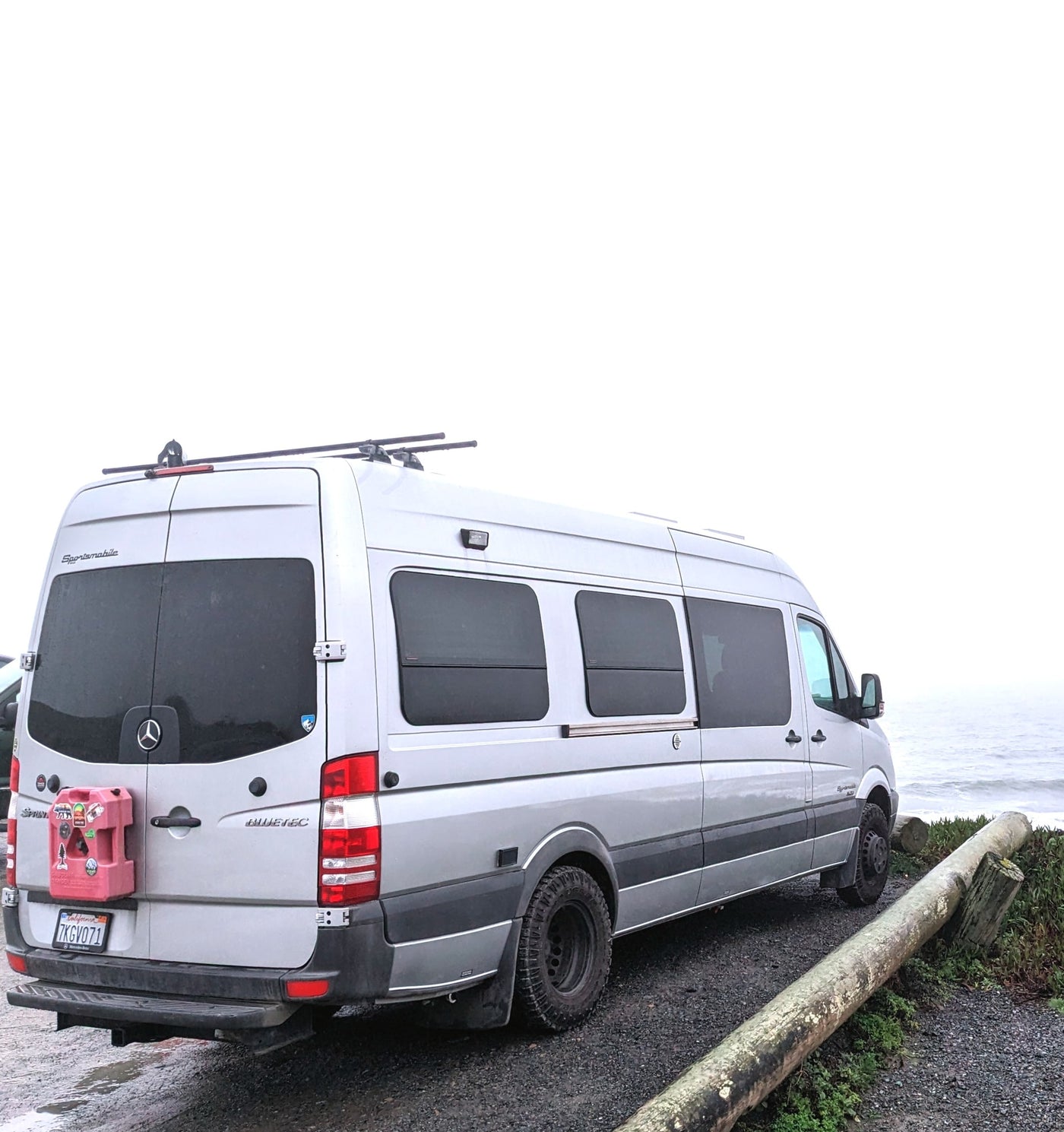  backed by a forested cliff.|Silver rv rental camper van parked on a mountain gravel road. Side door open — photo 7