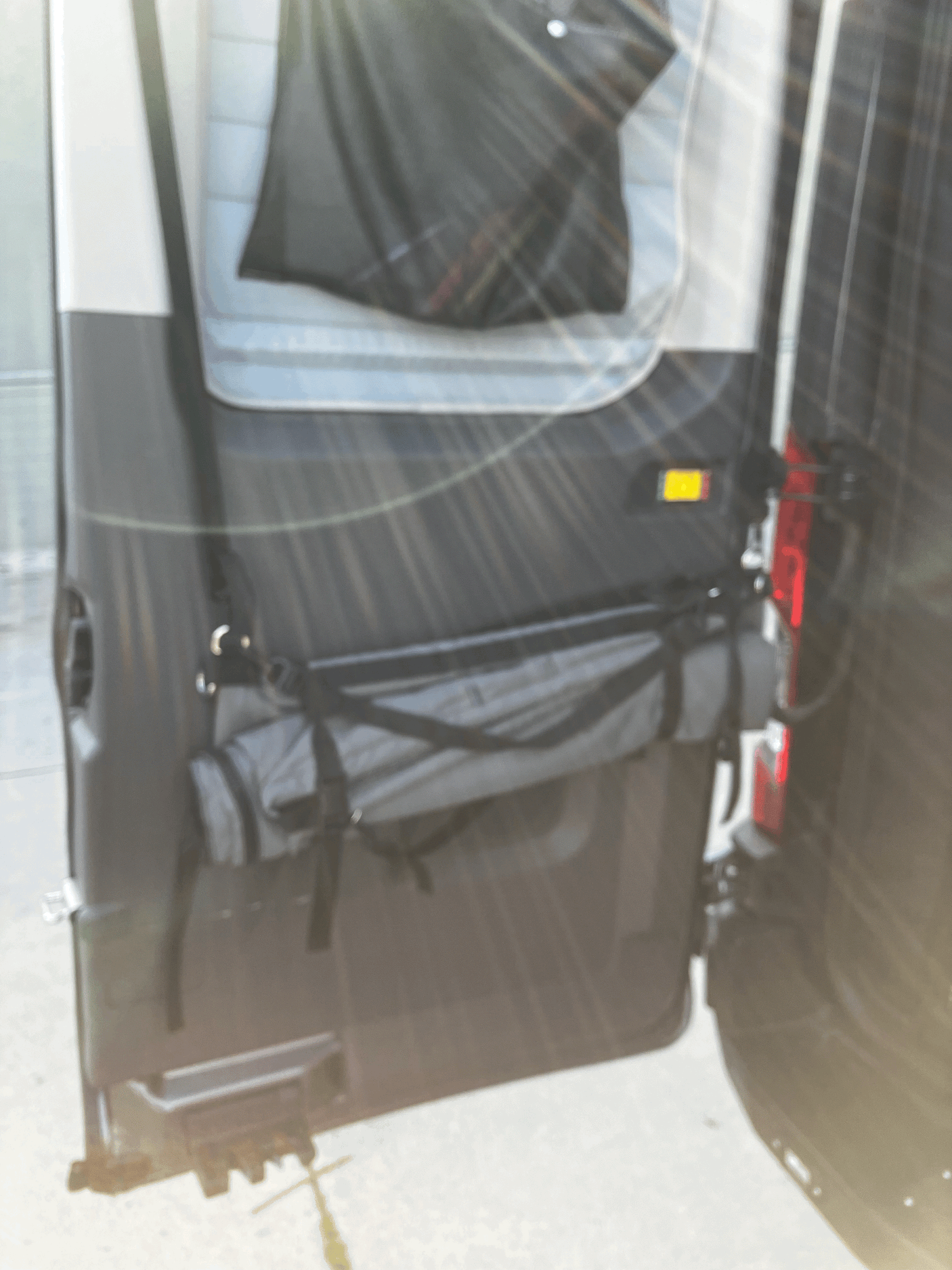 RV rental: Camper van's open back doors with interior organization, including a window cover & strapped rolled gear.