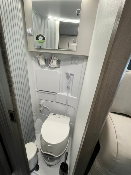 This rv rental features a compact, self-contained bathroom with a toilet, shower, and vanity mirror.