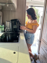 Smiling woman makes morning coffee in a modern rv rental kitchen, ready for road trip adventures. Compact and functional.