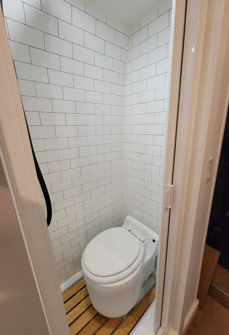 Inside an **rv rental**, this compact bathroom features white subway tiles, a toilet, and a wooden slat floor.