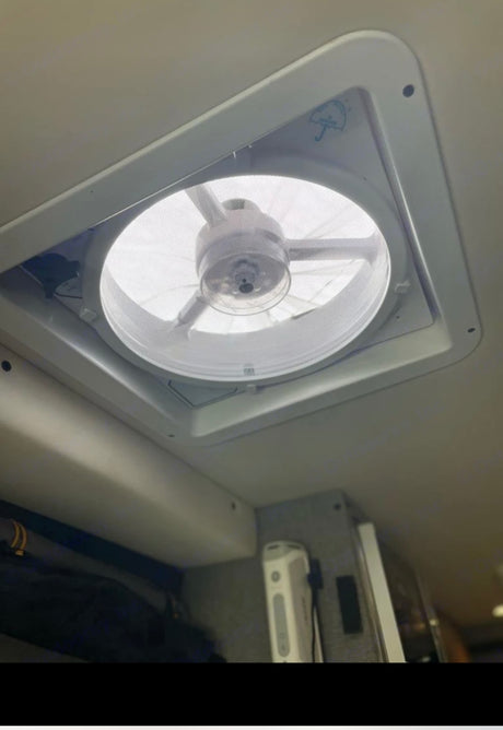 RV rental fan: The ceiling vent has a small umbrella icon, illuminated, with storage below in this camper van interior.