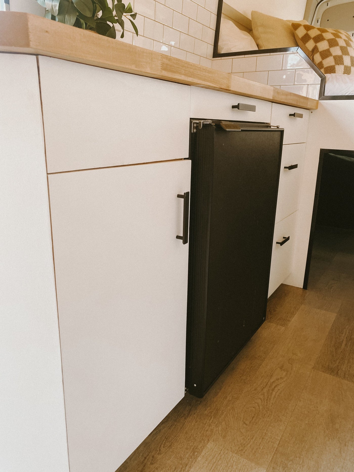 Sleek RV rental kitchen featuring white cabinets, a wooden countertop, and a built-in black refrigerator. Minimalist design. — photo 6