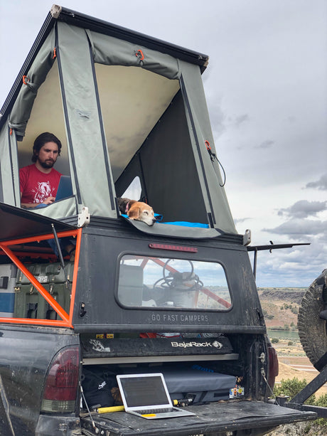Work remotely on an **RV rental**! Man and dog in a truck-top pop-up camper with laptops.