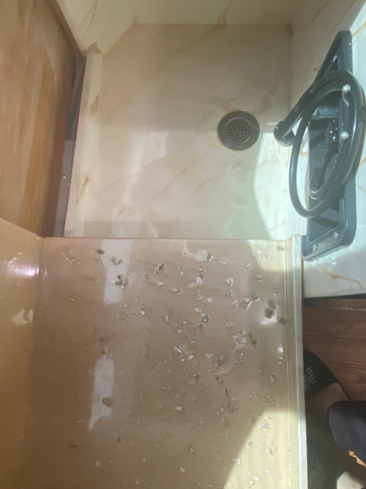 Compact beige shower in an RV rental, with drain, hose, and water marks. Showcases practical bathroom amenities.