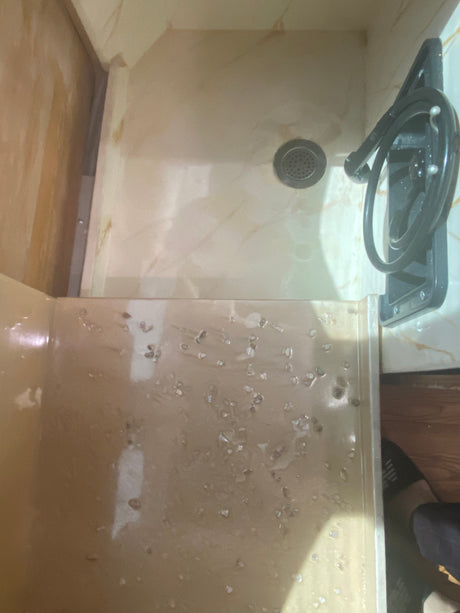 Compact beige shower in an RV rental, with drain, hose, and water marks. Showcases practical bathroom amenities.