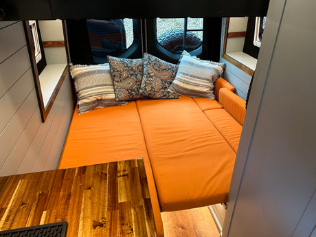 Cozy RV rental interior: Fold-out bed with orange cushions & decorative pillows for comfortable travel.
