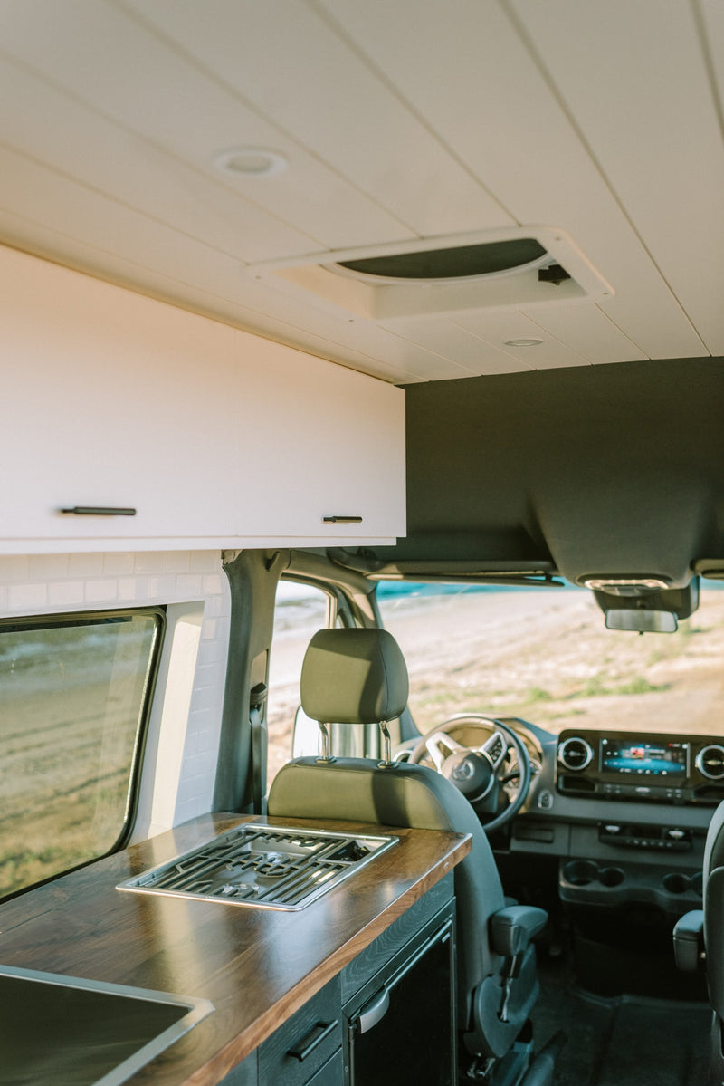 Experience an RV rental! This modern camper van features a full kitchen with stove, sink, wood counters, and driver's area. — photo 6