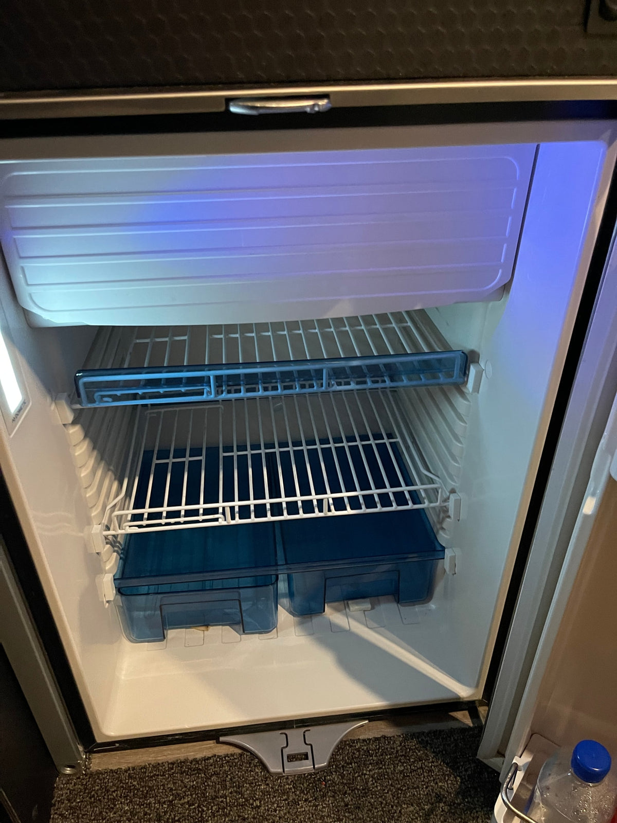 Empty, clean refrigerator in an **rv rental**, revealing wire shelves, blue storage bins, and bright interior lighting. — photo 7