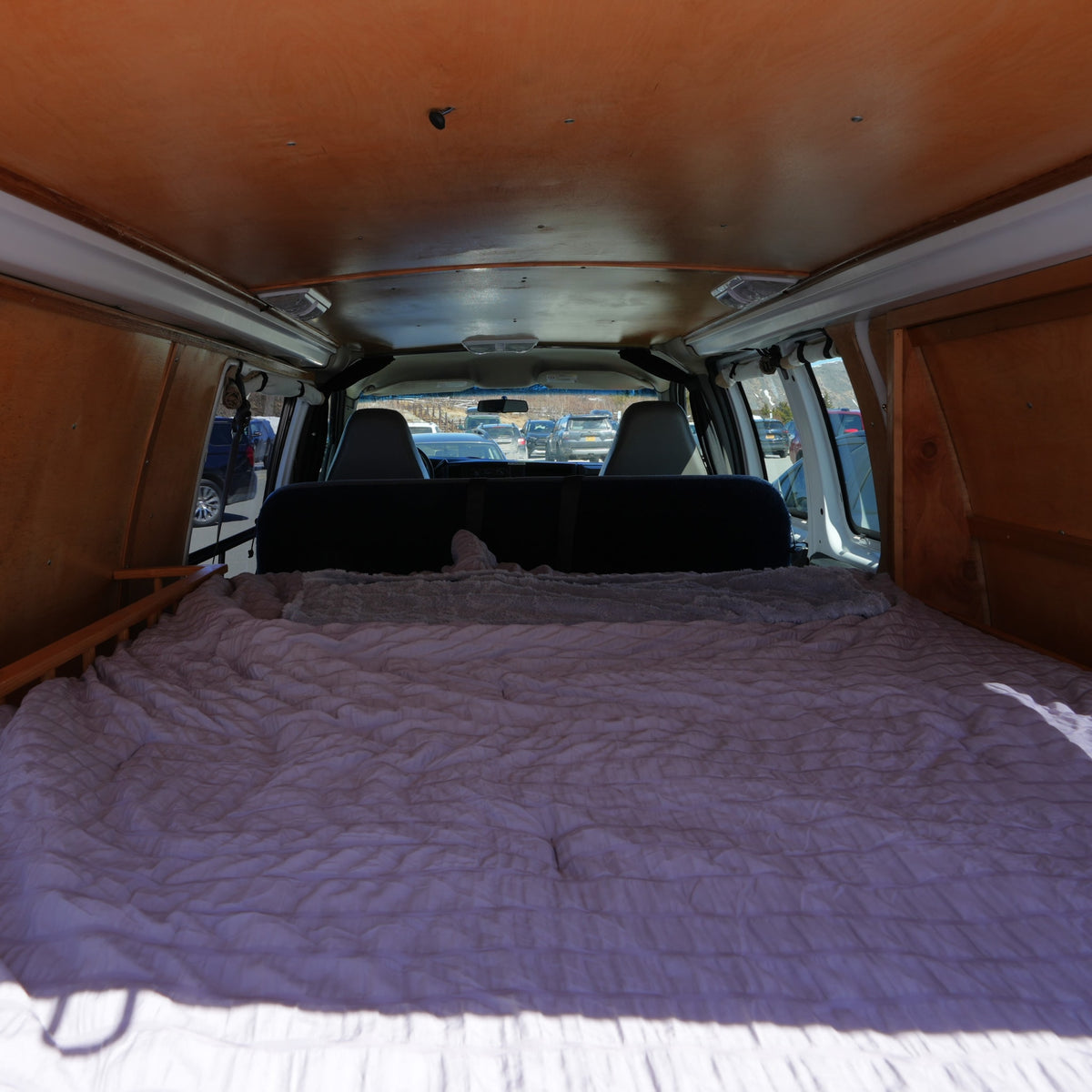 Inside a cozy RV rental: a plush bed in the rear, wooden paneling, and a view of parked cars through the front. — photo 11