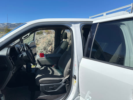 White pickup truck's interior view, perfect for an RV rental trip, with open doors and a distant RV in the mountainous landscape.
