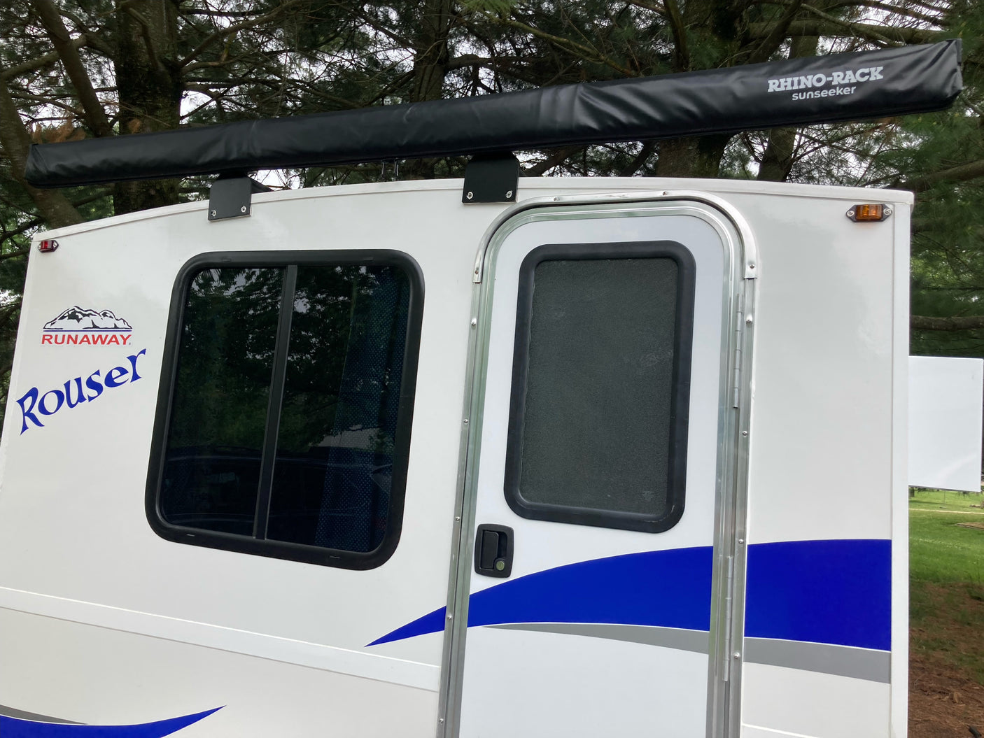 White Runaway Rouser RV rental showing its side profile with an attached Rhino-Rack awning, window, and door. Ready for travel.