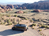 RV rental camper van with solar panels parked in a vast red rock desert. A person stands nearby, ready for off-grid adventures.