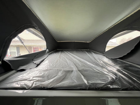 Pop-top RV rental: New sleeping loft, mattress wrapped in plastic, with residential views from side windows.