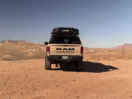 Tan RAM truck with rooftop tent parked on a dirt road in a desert landscape, ideal for an RV rental adventure.