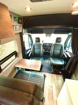 This RV rental's camper van interior features swiveled front seats, a dining table, rear bench, and controls.