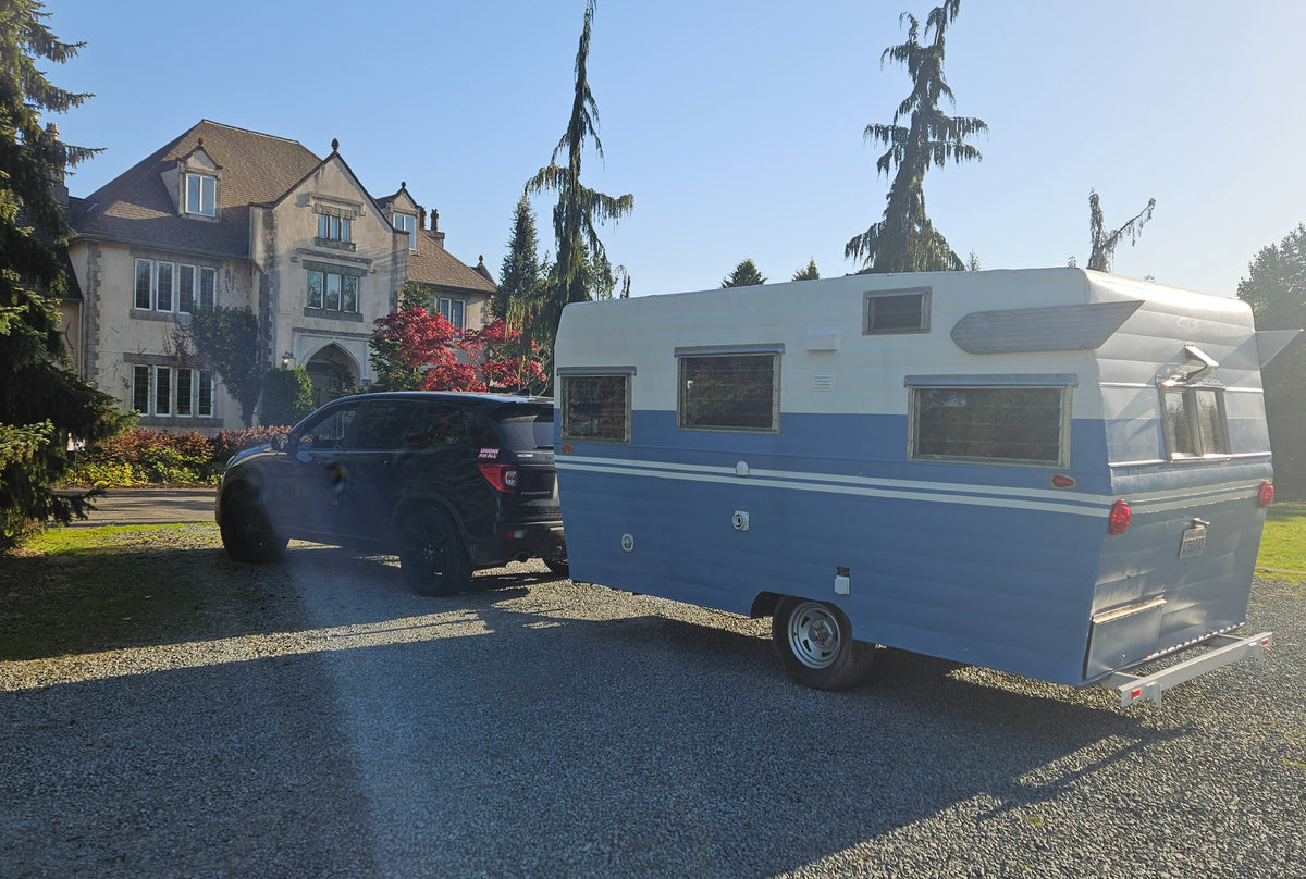An SUV tows a classic blue and white travel trailer on a gravel driveway in front of a large house. Great for an RV rental. — photo 2