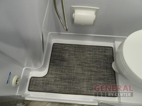 Compact RV rental wet bath interior with shower hose, toilet, and custom-fit gray floor mat.