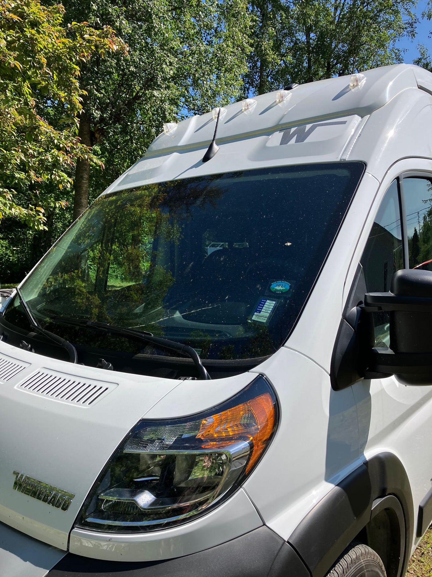 White Winnebago camper van, possibly for rv rental, parked outdoors among trees on a sunny day.