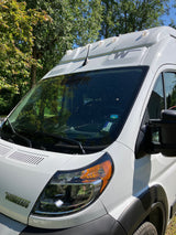 White Winnebago camper van, possibly for rv rental, parked outdoors among trees on a sunny day.