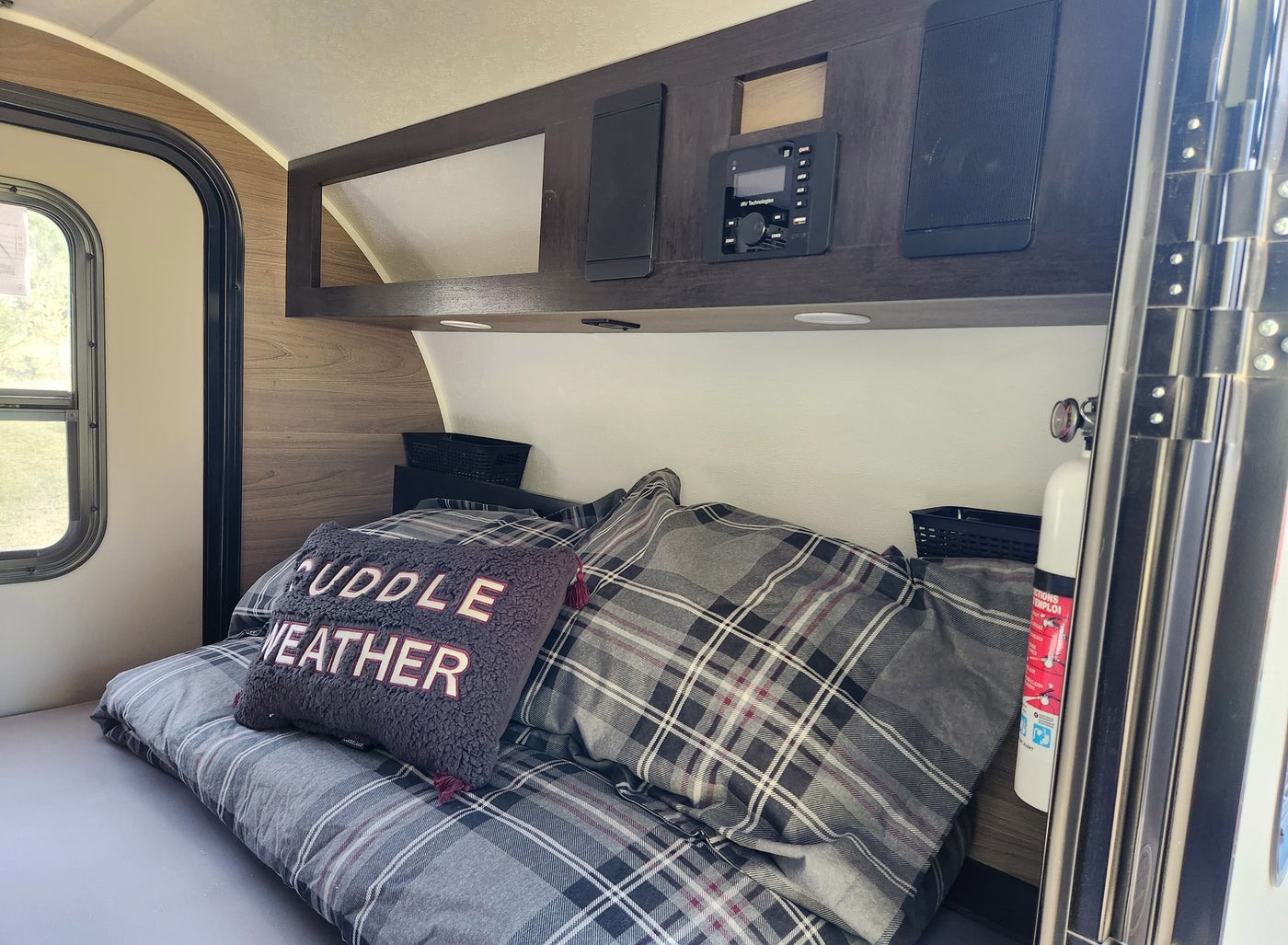 Cozy RV rental bedroom with plaid bedding, 'CUDDLE WEATHER' pillow, and overhead entertainment system. Ideal for travel. — photo 4
