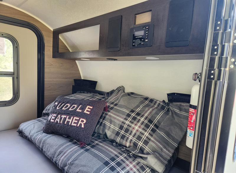 Cozy RV rental bedroom with plaid bedding, 'CUDDLE WEATHER' pillow, and overhead entertainment system. Ideal for travel. — photo 4